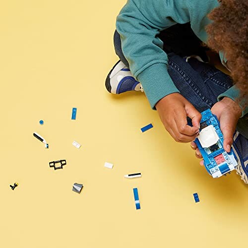 Child assembling a blue LEGO car on a yellow background.