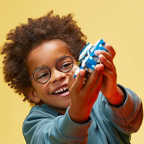 Child smiling and holding a blue toy car against a yellow background.