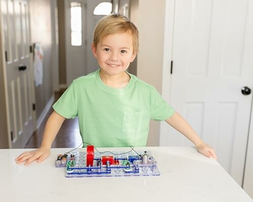 Smiling child with an electronics kit on a table.